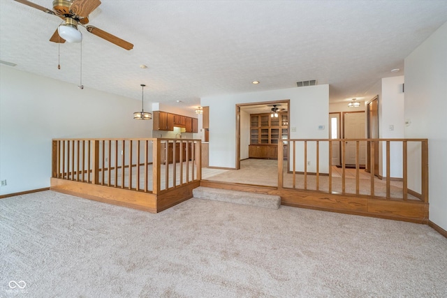 unfurnished living room with light colored carpet, baseboards, ceiling fan, and visible vents