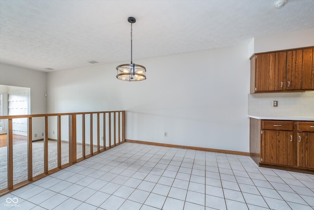 interior space featuring an inviting chandelier, decorative backsplash, light countertops, a textured ceiling, and brown cabinets
