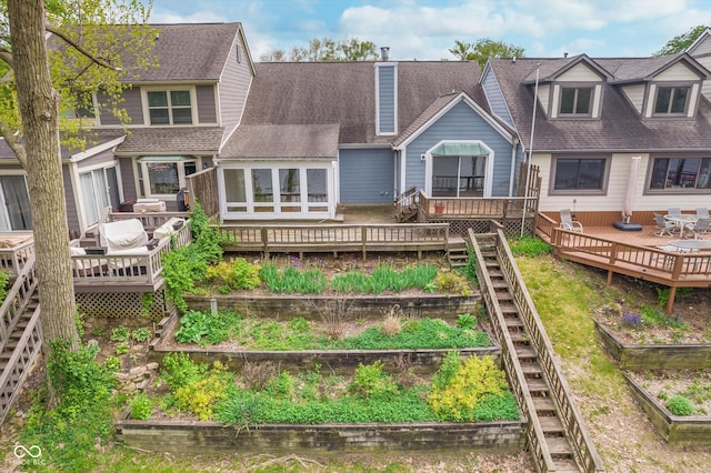 back of house featuring a wooden deck, a shingled roof, and a vegetable garden