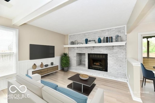living room with wainscoting, wood finished floors, a fireplace, and beamed ceiling