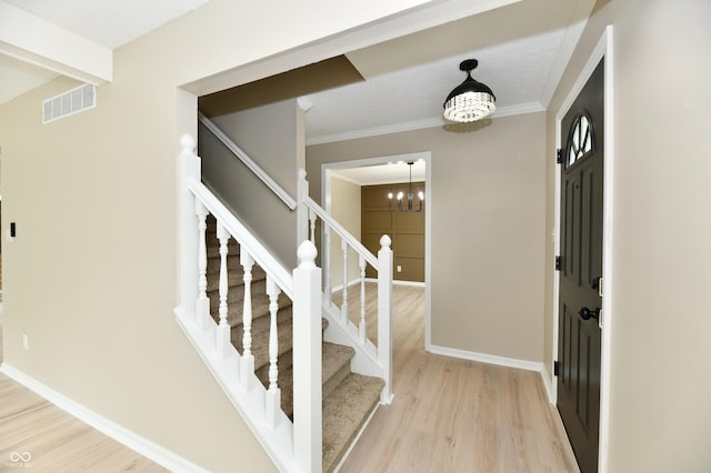 entrance foyer with visible vents, crown molding, stairway, light wood-type flooring, and a chandelier