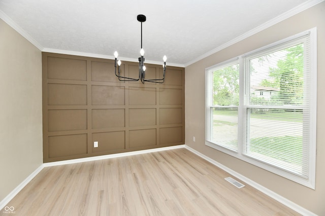 unfurnished dining area with baseboards, a notable chandelier, light wood-style floors, ornamental molding, and a decorative wall