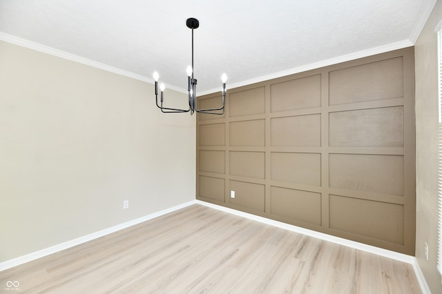 unfurnished dining area with light wood-style floors, an inviting chandelier, a decorative wall, and crown molding
