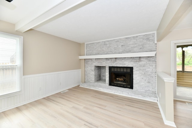 unfurnished living room with visible vents, wood finished floors, a fireplace, beamed ceiling, and a wainscoted wall