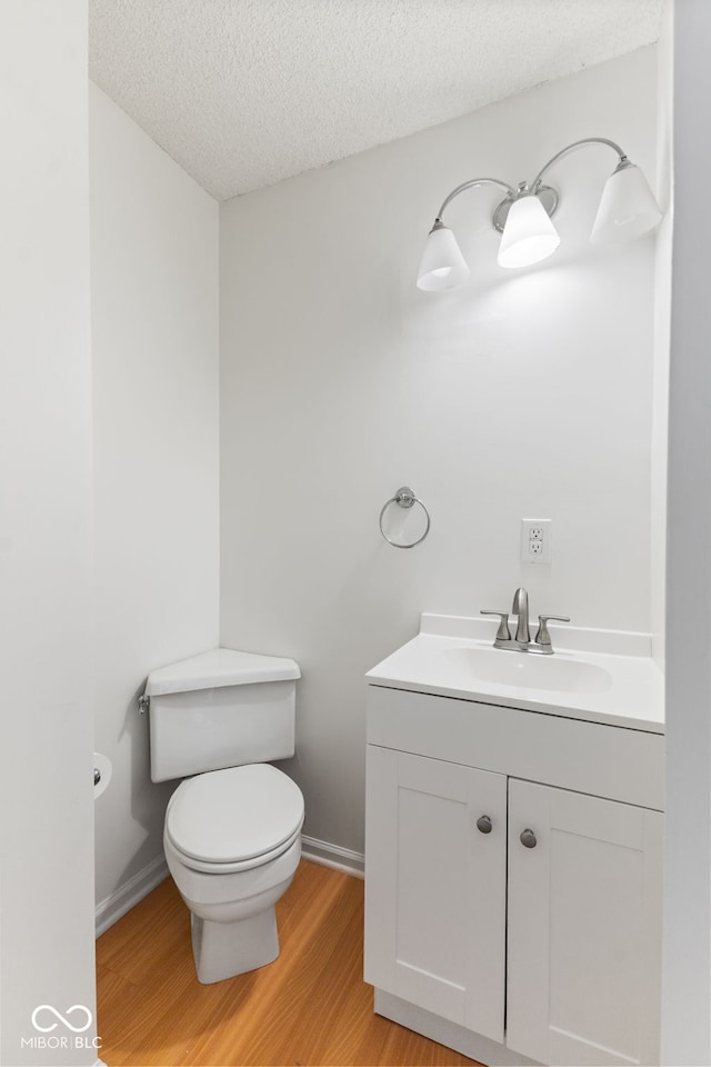 half bath with vanity, a textured ceiling, toilet, and wood finished floors