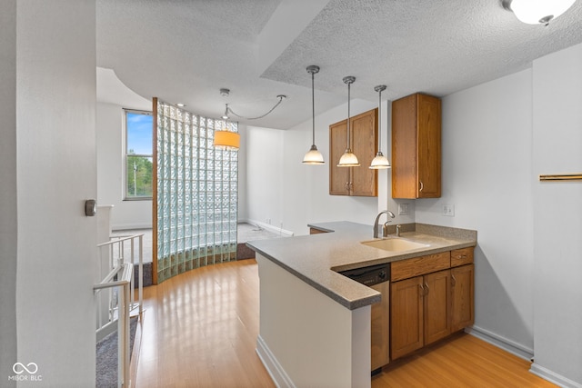 kitchen with hanging light fixtures, a sink, light wood-style floors, brown cabinetry, and stainless steel dishwasher