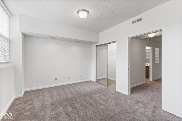unfurnished bedroom featuring multiple windows, carpet, a textured ceiling, and visible vents