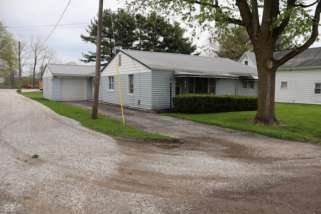 view of front facade with an outbuilding, driveway, metal roof, and a front yard
