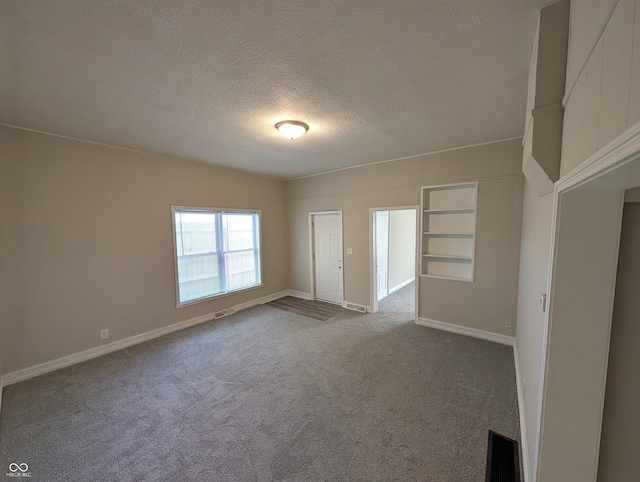empty room with visible vents, a textured ceiling, dark carpet, and baseboards