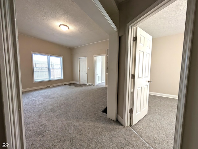 carpeted empty room with baseboards, a textured ceiling, and visible vents