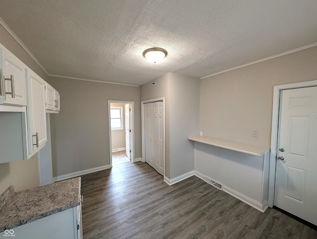 unfurnished dining area with visible vents, ornamental molding, a textured ceiling, and dark wood finished floors