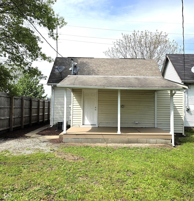 back of property featuring fence, a shingled roof, a lawn, and a porch