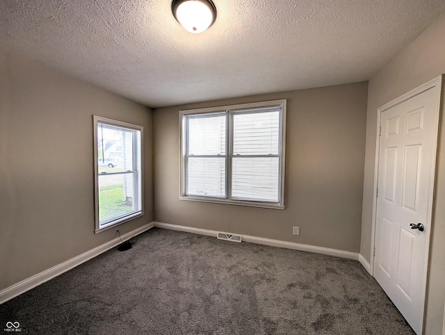spare room with a wealth of natural light, dark carpet, a textured ceiling, and visible vents