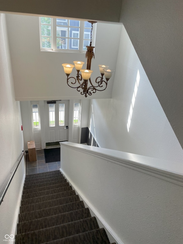 stairway with an inviting chandelier, tile patterned flooring, and a healthy amount of sunlight