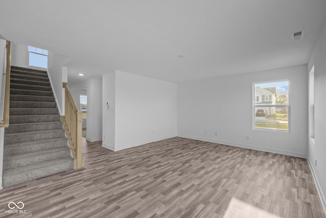 unfurnished living room with light wood-type flooring, baseboards, visible vents, and stairway