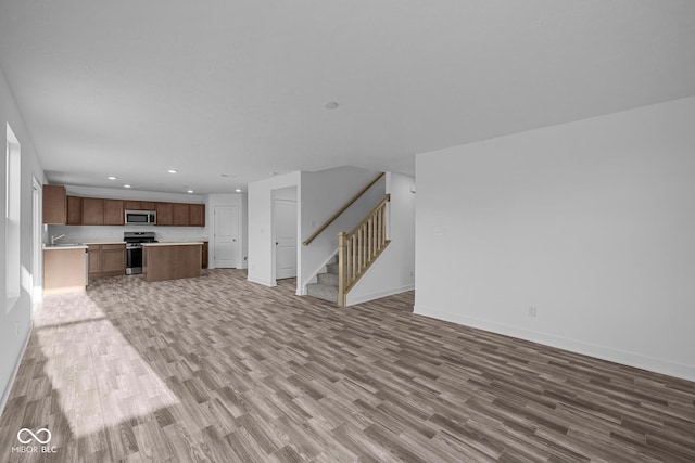 unfurnished living room featuring light wood-style floors, baseboards, and stairway
