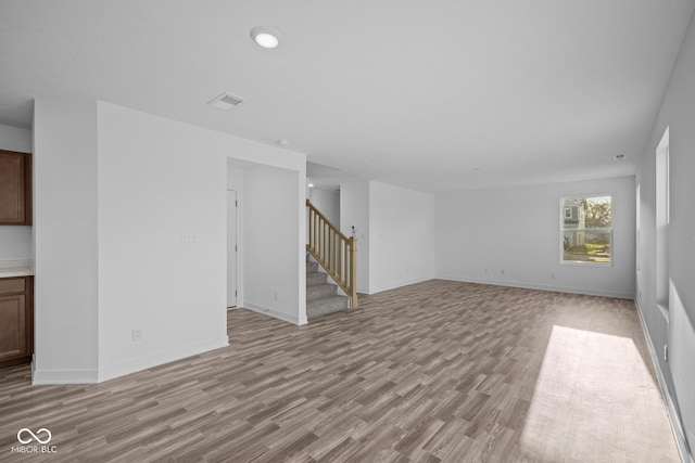 unfurnished living room featuring baseboards, light wood-type flooring, stairs, and visible vents