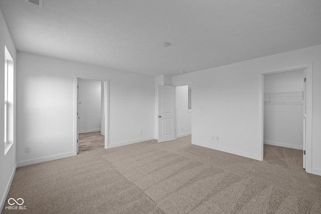 unfurnished bedroom with a closet, light carpet, baseboards, a walk in closet, and a textured ceiling