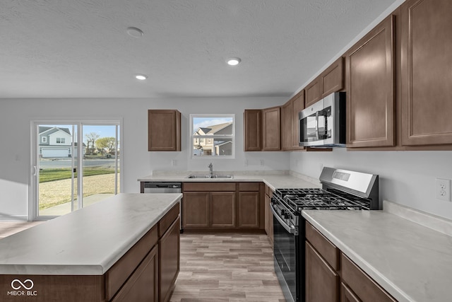 kitchen with a sink, appliances with stainless steel finishes, light wood-style floors, and light countertops