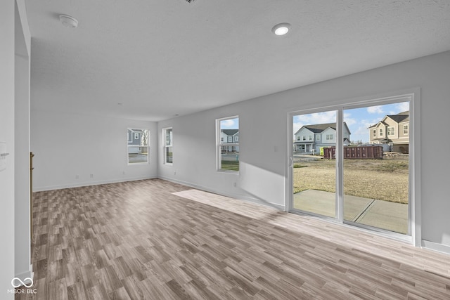 unfurnished living room with baseboards, a textured ceiling, and wood finished floors
