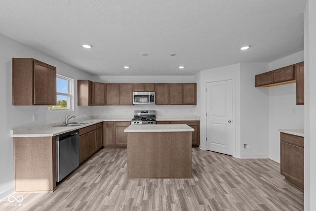 kitchen with appliances with stainless steel finishes, a sink, light wood finished floors, light countertops, and a center island