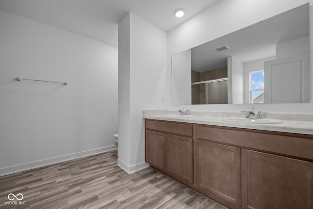 bathroom featuring a sink, a shower stall, wood finished floors, and visible vents