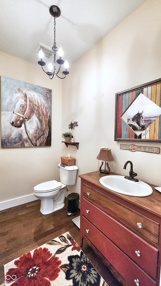 half bathroom with an inviting chandelier, vanity, toilet, wood finished floors, and visible vents