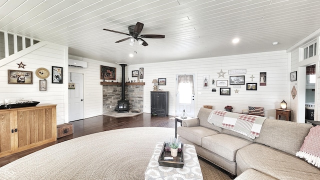 living area with wooden walls, a wall unit AC, a wood stove, and dark wood-style flooring