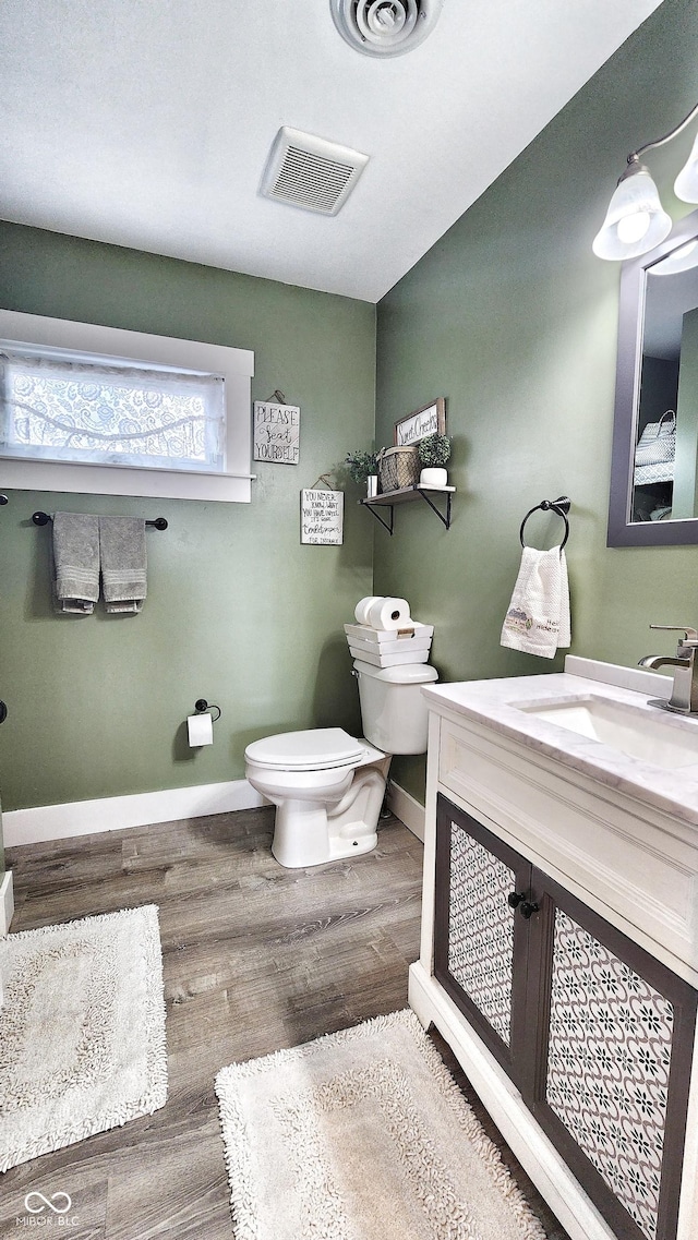 bathroom with toilet, baseboards, visible vents, and wood finished floors
