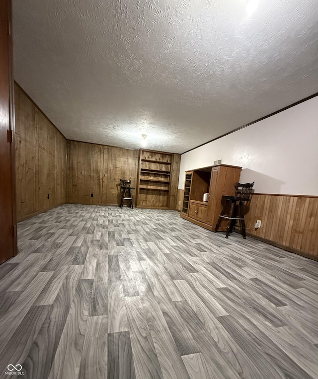 additional living space with a textured ceiling, built in features, wainscoting, light wood-type flooring, and wooden walls