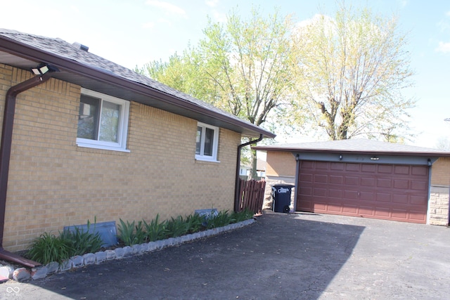 view of property exterior with brick siding, an outdoor structure, and aphalt driveway