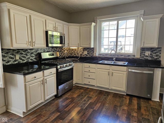 kitchen featuring a sink, appliances with stainless steel finishes, dark wood-style flooring, and dark countertops