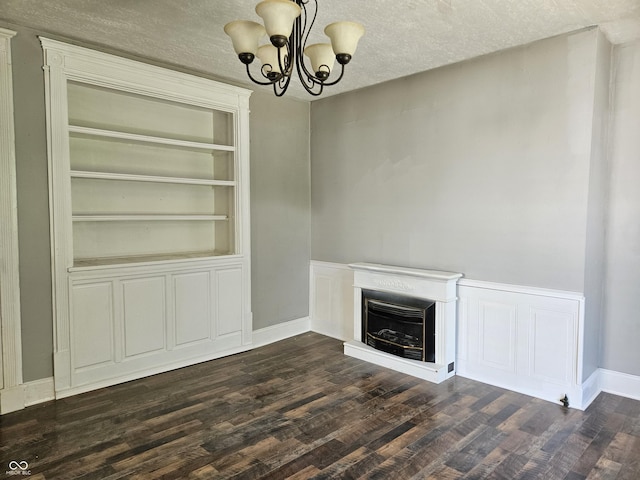 unfurnished living room featuring baseboards, dark wood finished floors, a notable chandelier, and a fireplace