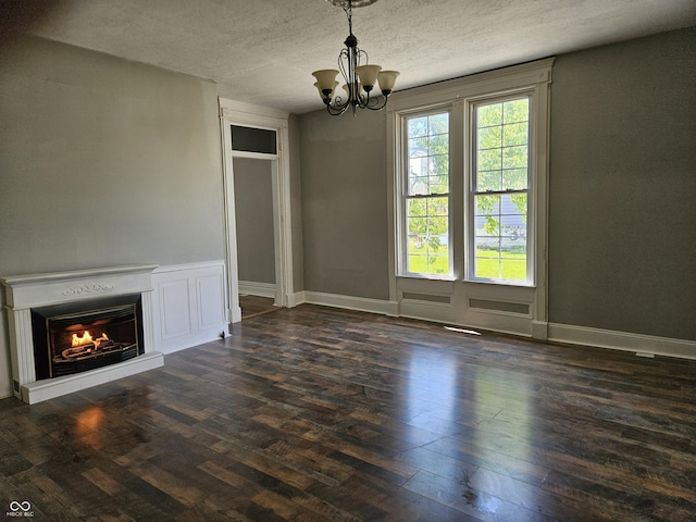 unfurnished dining area with a warm lit fireplace, an inviting chandelier, a textured ceiling, baseboards, and wood finished floors