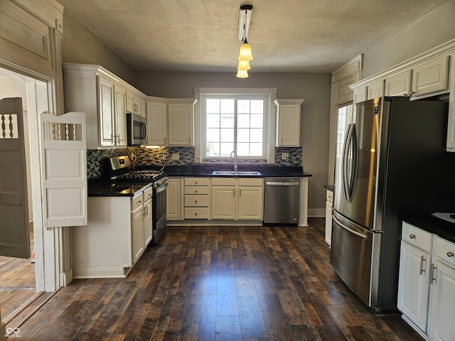 kitchen with stainless steel appliances, dark countertops, dark wood-style floors, and a sink