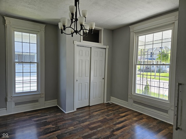 unfurnished dining area with an inviting chandelier, baseboards, a textured ceiling, and dark wood-type flooring