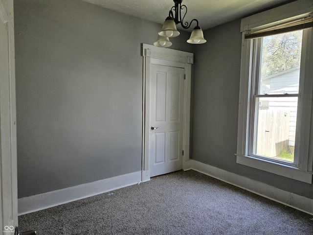 empty room featuring carpet floors, baseboards, a healthy amount of sunlight, and an inviting chandelier