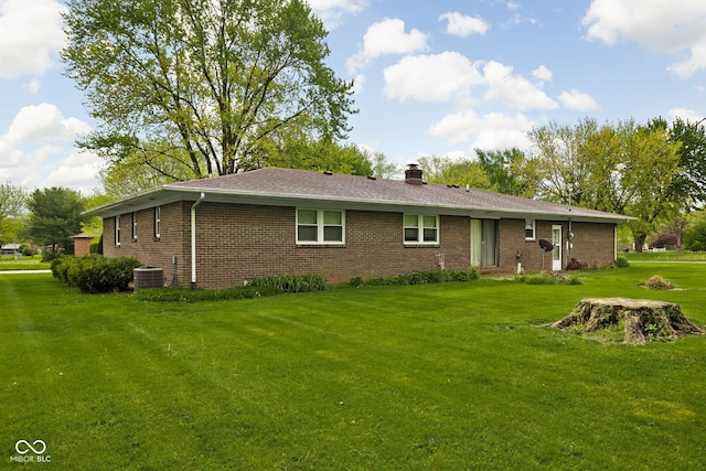 back of house with a yard, brick siding, a chimney, and central air condition unit