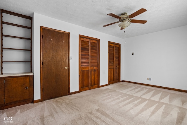 unfurnished bedroom featuring baseboards, a textured ceiling, two closets, and light carpet