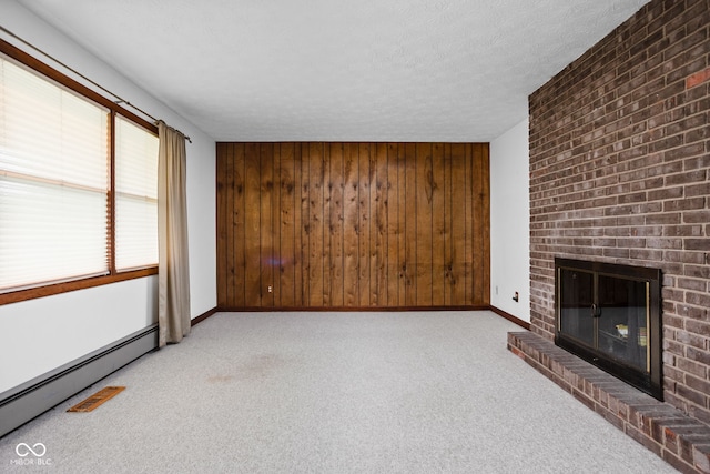 unfurnished living room with wooden walls, baseboard heating, a fireplace, carpet, and baseboards