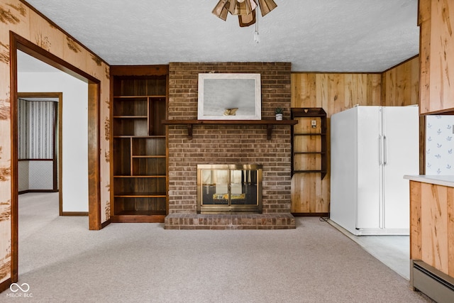 unfurnished living room featuring a ceiling fan, wood walls, a brick fireplace, a textured ceiling, and carpet flooring