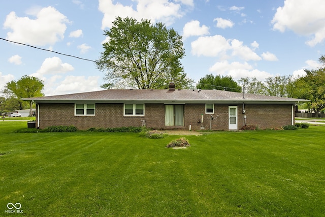 back of house featuring brick siding, a lawn, and a chimney