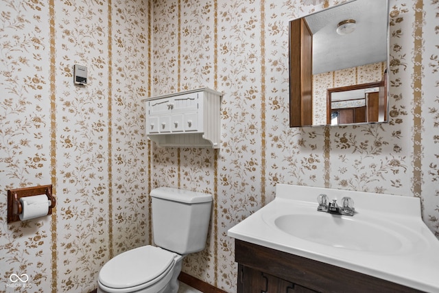 half bath with toilet, wallpapered walls, baseboards, and vanity