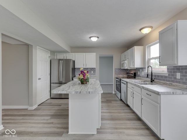 kitchen with decorative backsplash, appliances with stainless steel finishes, a center island, a sink, and white cabinets