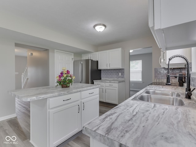 kitchen with decorative backsplash, light wood-type flooring, a sink, white cabinets, and freestanding refrigerator