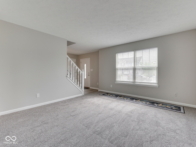 unfurnished living room featuring baseboards, carpet, and stairway