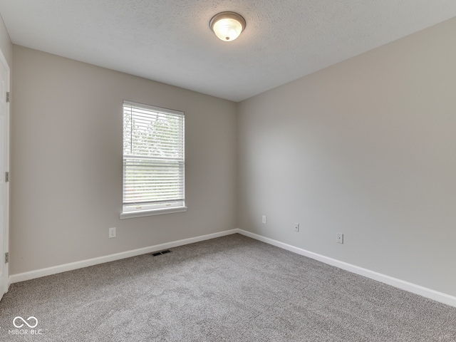 empty room with carpet floors, a textured ceiling, baseboards, and visible vents