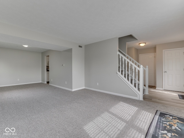 unfurnished living room featuring baseboards, carpet flooring, visible vents, and stairway