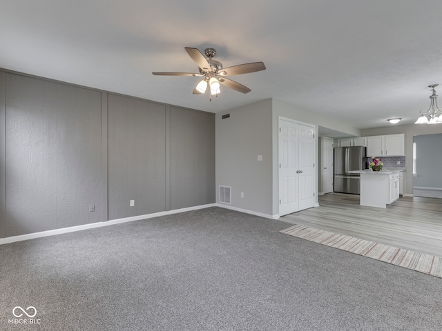 unfurnished living room with baseboards, ceiling fan with notable chandelier, light colored carpet, and visible vents