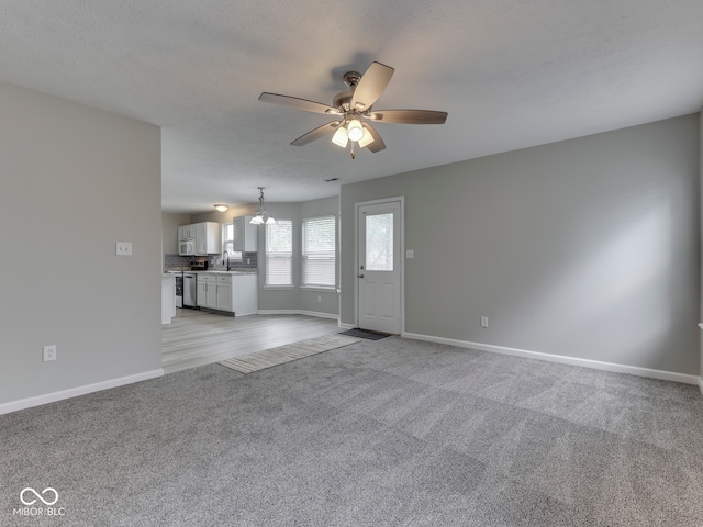 unfurnished living room featuring baseboards, a sink, ceiling fan with notable chandelier, and light colored carpet